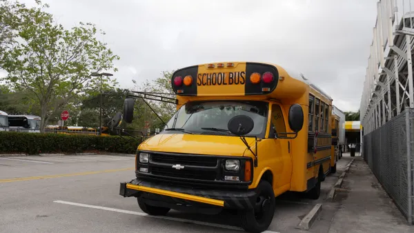 A yellow school bus is parked in a lot outside a school building.