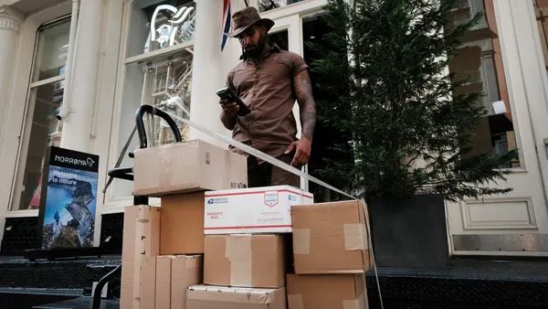 A UPS worker stands above a cart of packages on a sidewalk.