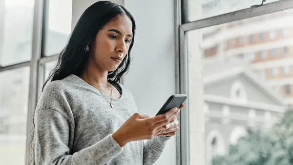 A woman checks her phone in front of a window.