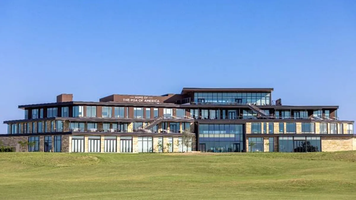 A large building is in the background with blue sky above and grass below. The building has large windows and is wrought out of stone.