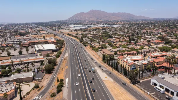 A multilane freeway in California with urban housing and a hillside range in the background.