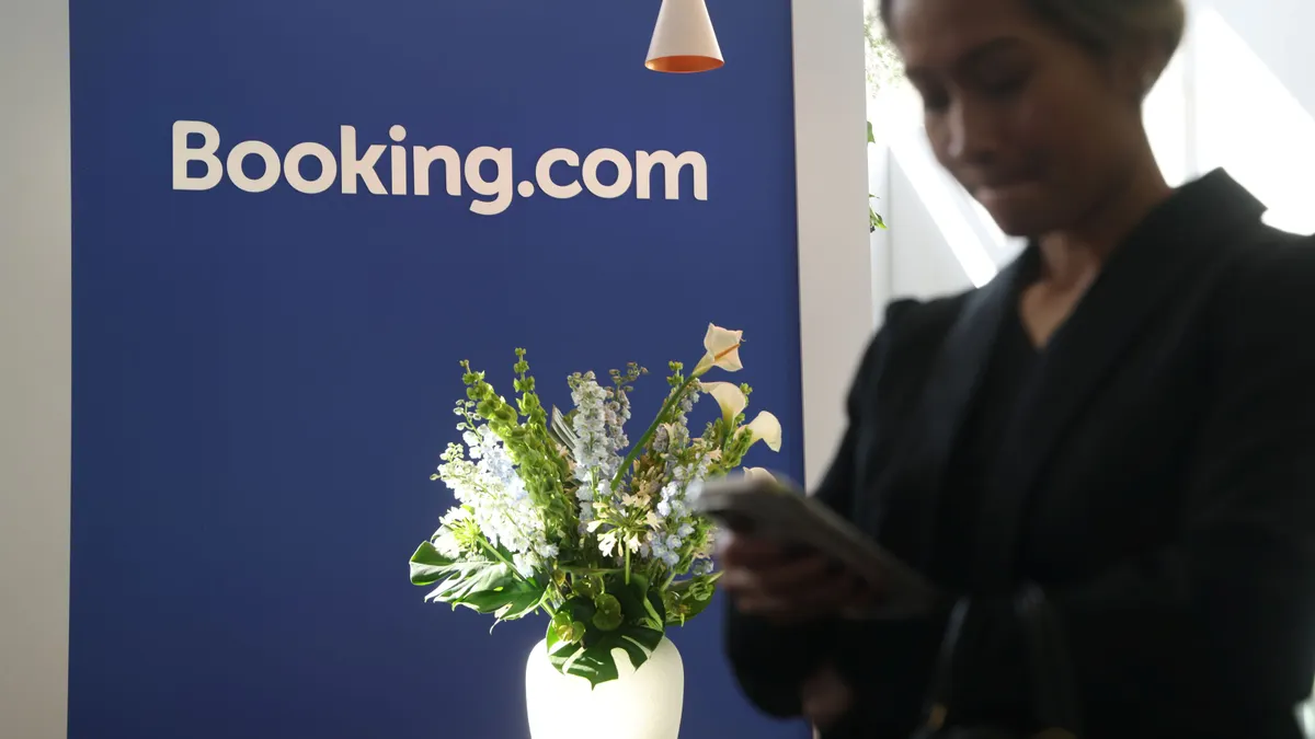 A person uses their phone in front of a Booking.com sign.