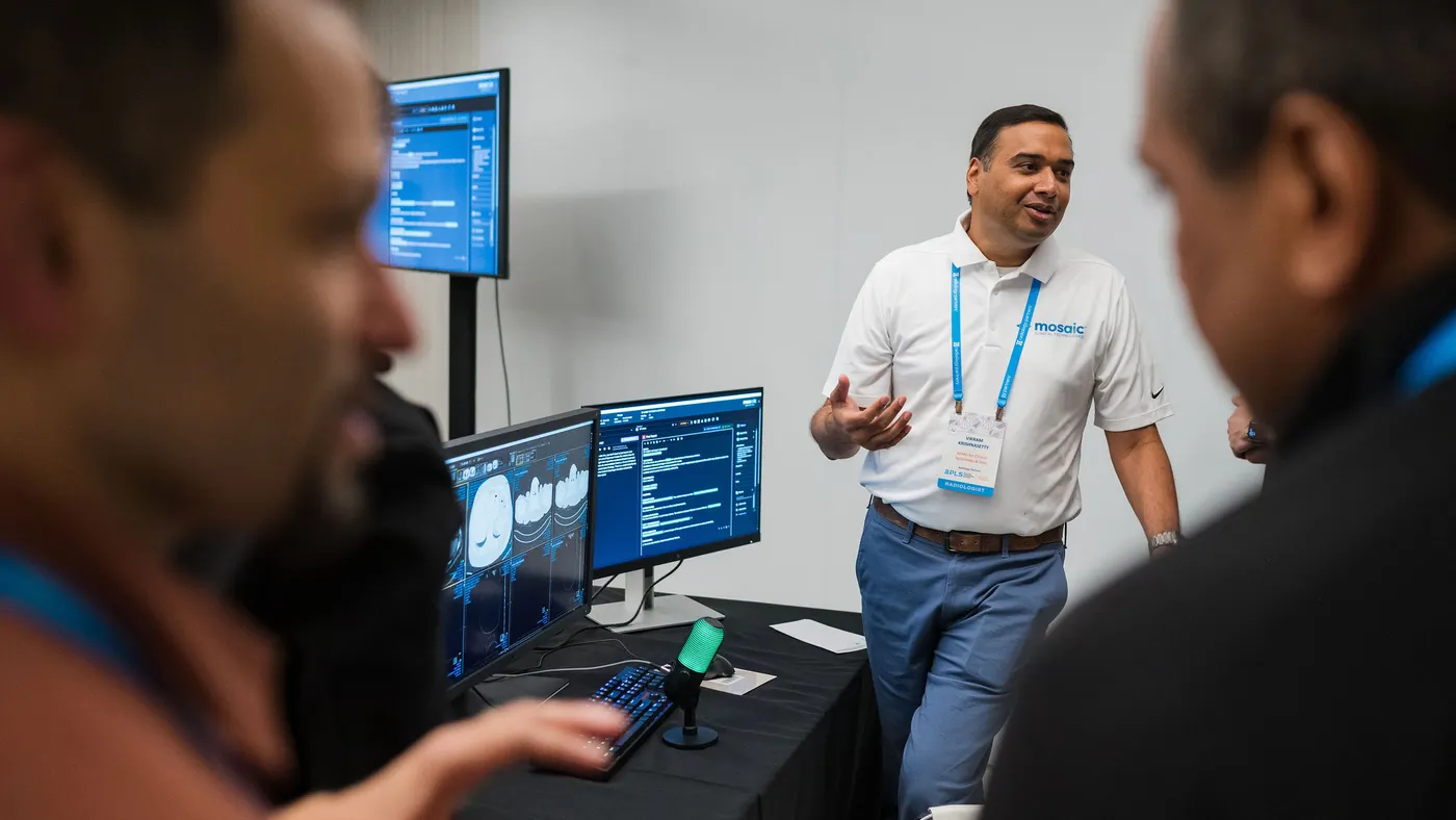 A person wearing a shirt that says "Mosaic" stands and speaks in front of two computer screens showing text and images.