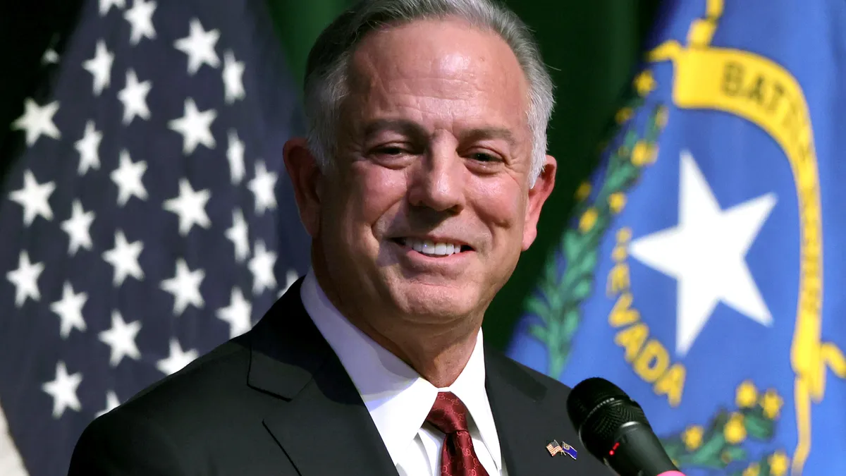 Nevada Gov. Joe Lombardo standing in front of microphone with American and Nevada flags behind him