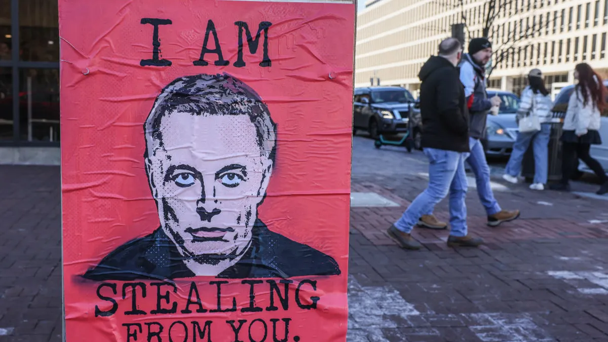 A poster outside the Education Department's building reading, in all caps, "I am stealing from you," with an illustration of Elon Musk in the center.