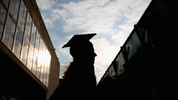 A backlit silhouette of a student wearing a cap and gown