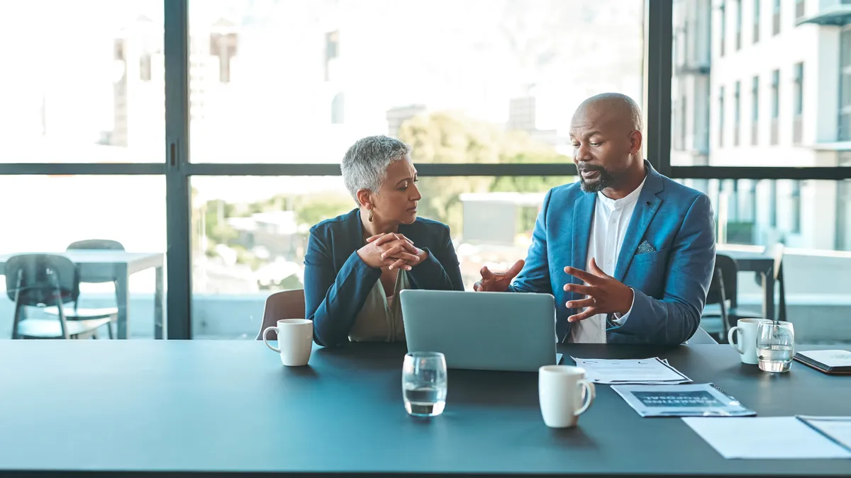 A general counsel and CFO have a discussion while seated at a table