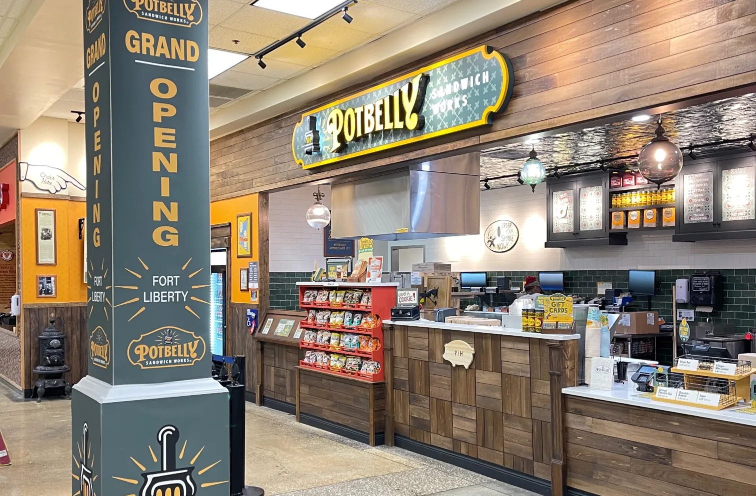 A Potbelly storefront with green decor. A pillar says grand opening.