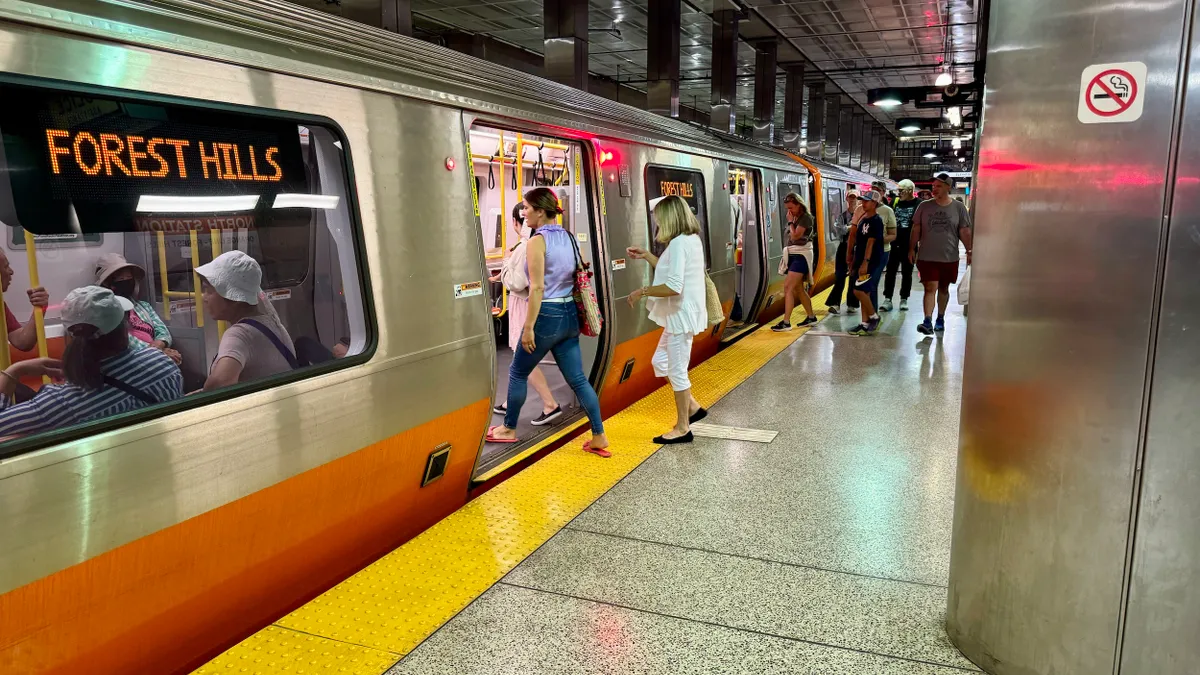 People in an underground subway station board a silver and orange train.