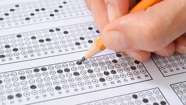 A hand is holding a pencil that is shading in bubbles on a test sheet