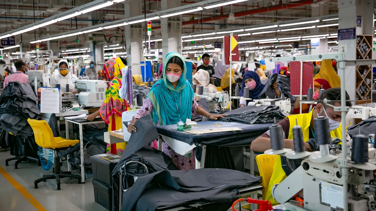 A factory with rows of Bangladeshi garment workers behind their sewing machines working on fashion garments