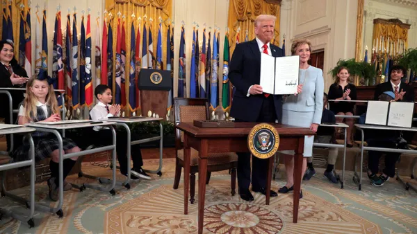 President Donald Trump stands next to Linda McMahon while holding the executive order in the White House.