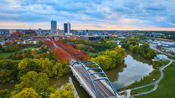 Golden hour captures autumn's vibrant hues in Fort Wayne, Indiana, featuring the modern Martin Luther King Bridge over a serene river with downtown skyline backdrop.