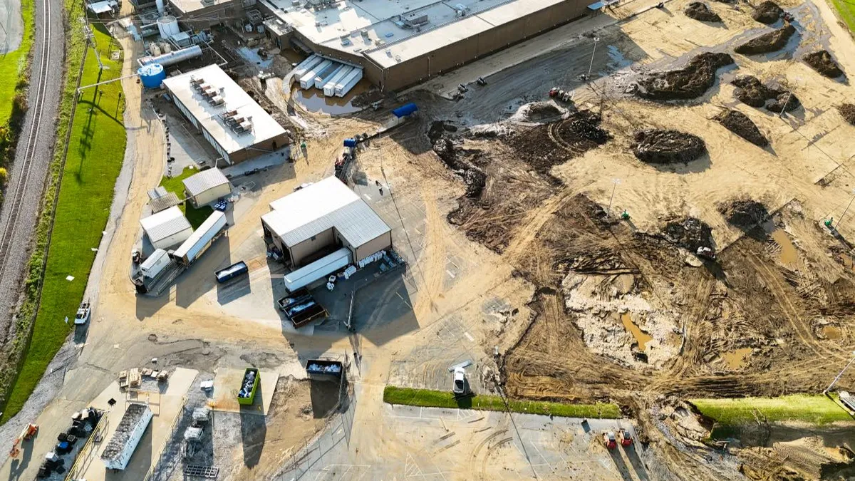 An aerial view shows a large plant surrounded by trucks, mounds of dirt and pools of water.