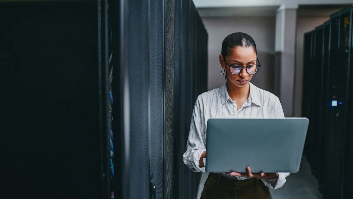 Shot of a young woman using a laptop while working in a server room.