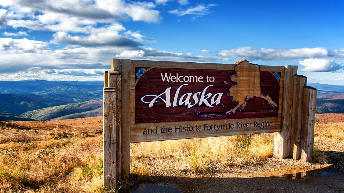 A Welcome to Alaska sign stands beside a highway.