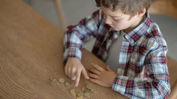 A young boy sits at a table counting coins