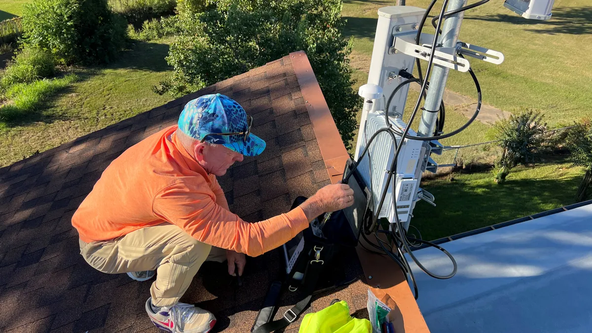 A man installs WiFi network equipment on a building's roof.