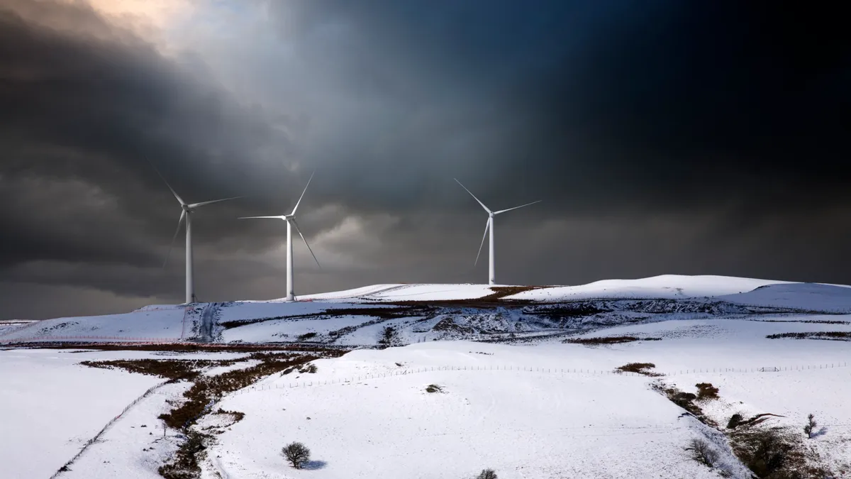 Three wind turbines on a snow-covered hill on the edge of the Snowdonia National Park, Wales.