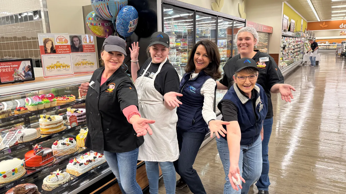 A group of people standing next to a bakery counter in a grocery store.