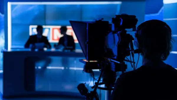 A camera operator films two TV news anchors in a broadcast studio