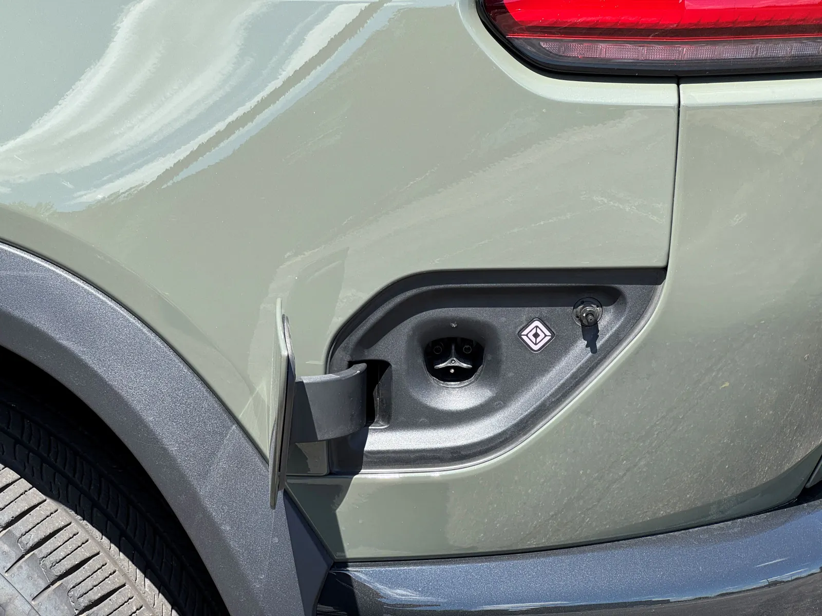 An open electric vehicle charging port is shown. To the right of the charging port is Rivian's diamond-shaped logo.