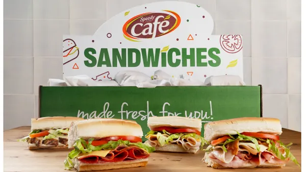 A photo of several sandwiches on a wooden table with a green and white box behind them that says Speedy Cafe Sandwiches.