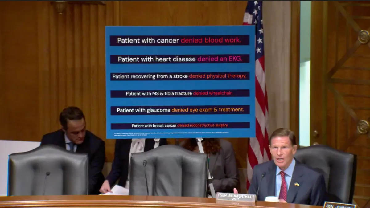 Senator Richard Blumenthal sits in front of a poster illustrating Medicare Advantage coverage denials