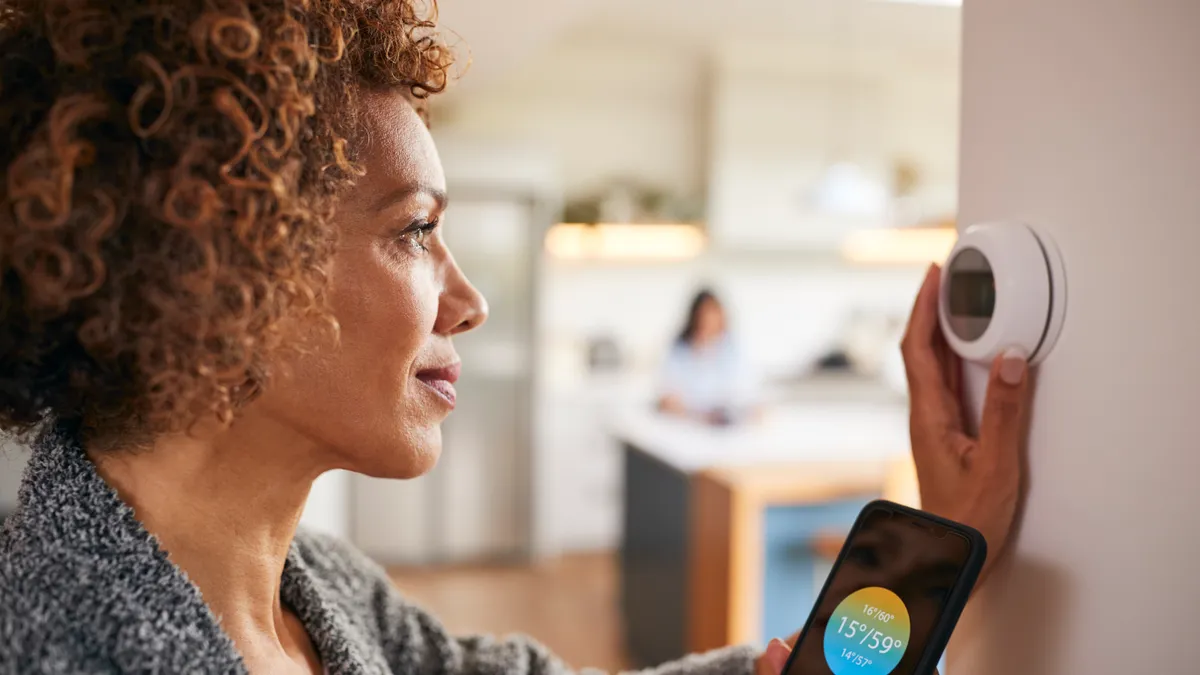 Woman using app on Phone to control digital central heating thermostat at home