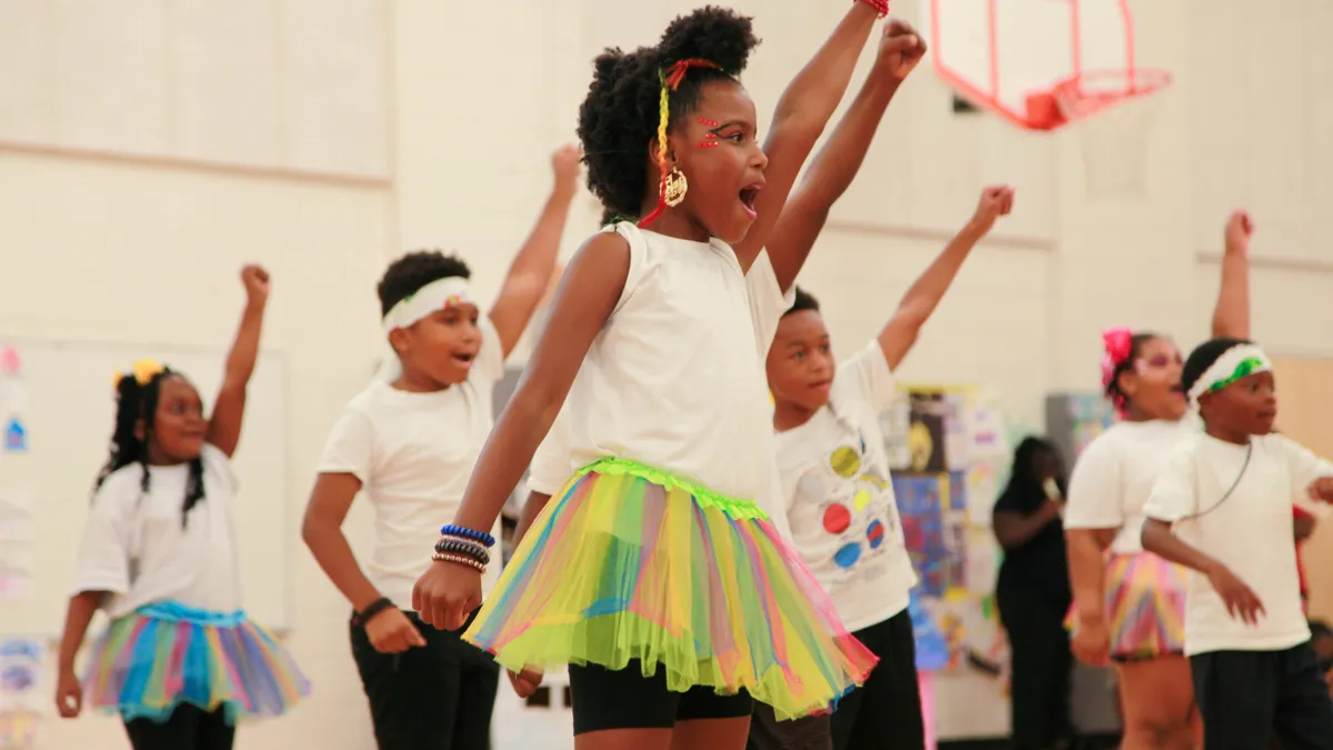 A group of children participate in a dance activity in a gymnasium during a summer learning program.