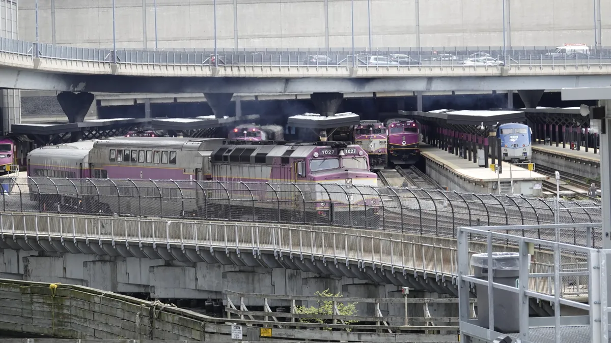 Purple and silver commuter trains fill tracks at a large train station in Boston, as one approaches the camera leaving the station.