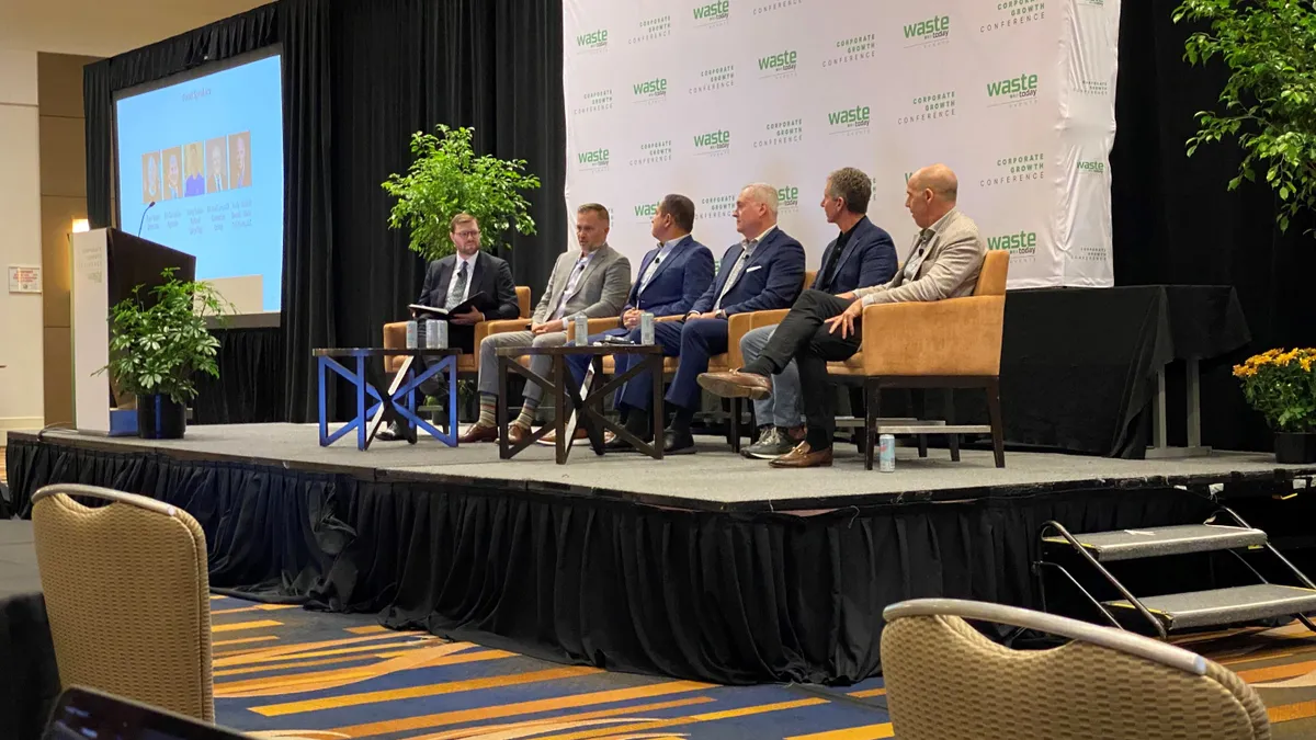 A group of men sit on a stage at a conference with a backdrop that reads "Corporate Growth Conference" and "Waste Today events."