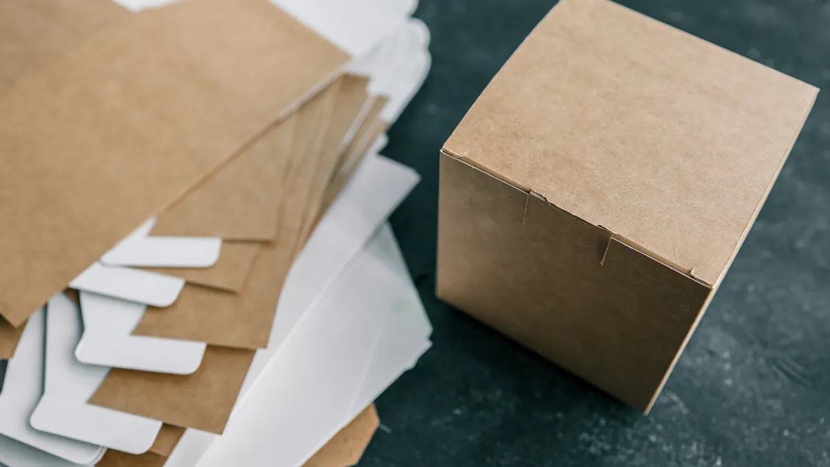 A stack of unfolded, flat paperboard boxes next to one folded box.