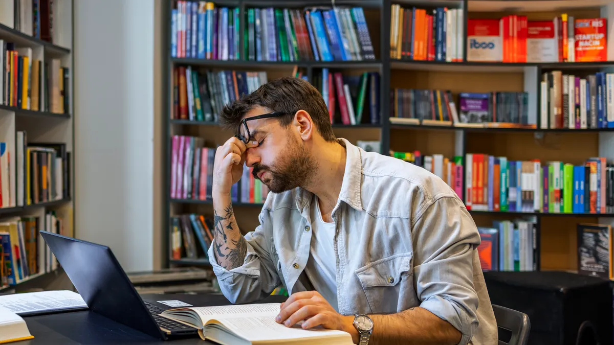 A person sits at a desk with his hand on his head, looking stressed.