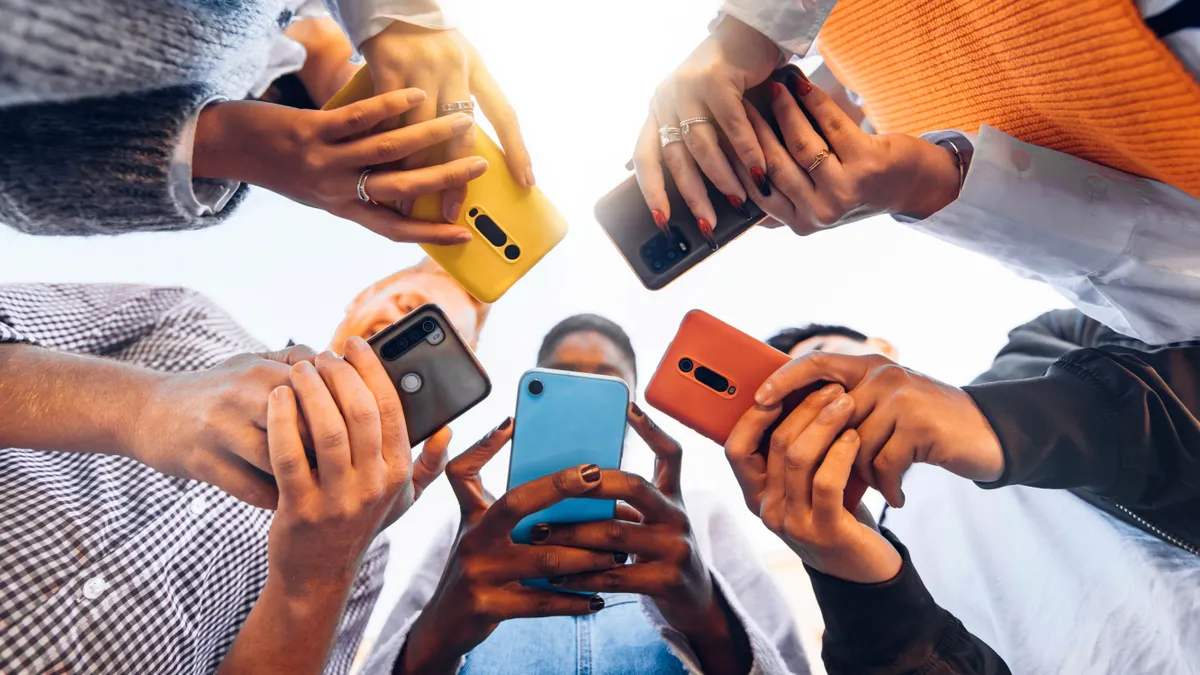 Teens in circle holding smart mobile phones of different colors.