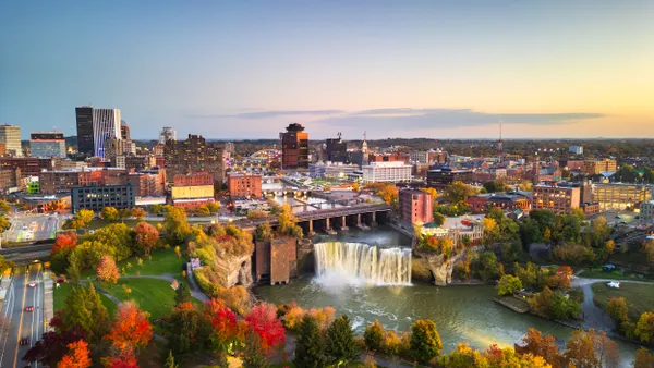 Aerial view of city with river and waterfall in the center and trees turning fall colors.