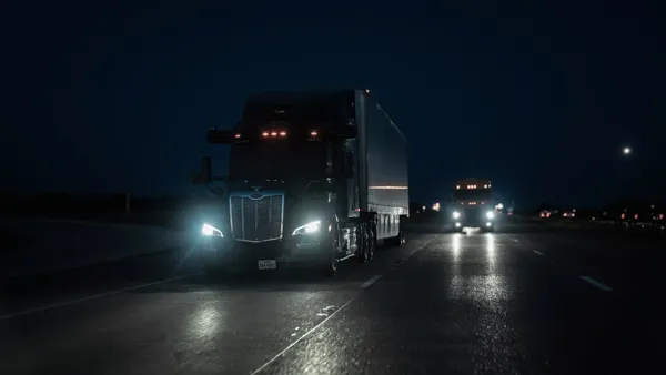 An Aurora-equipped driverless truck with headlights on at night.