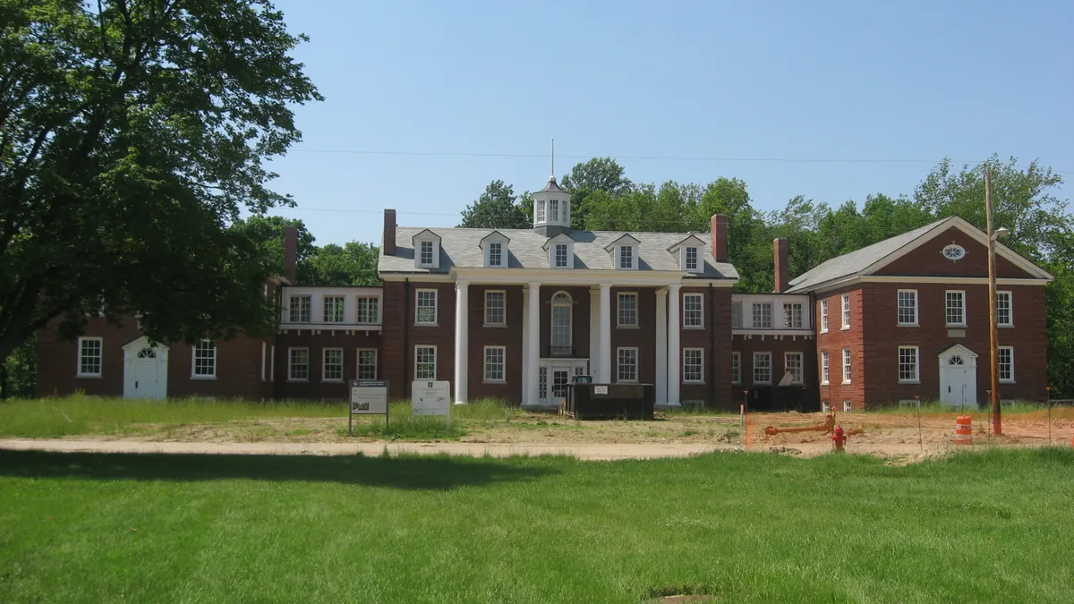 A brick hall with white columns seen from the front with construction barricades.