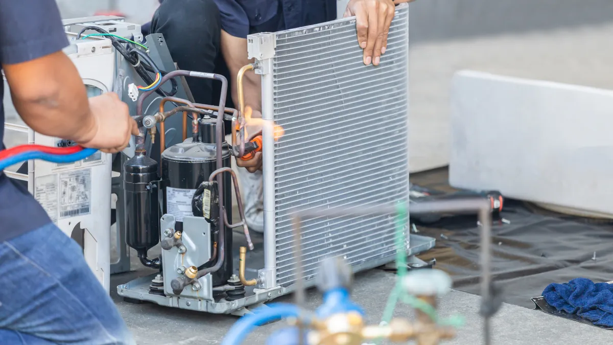 Two people are seen fixing the inside of an air conditioning unit