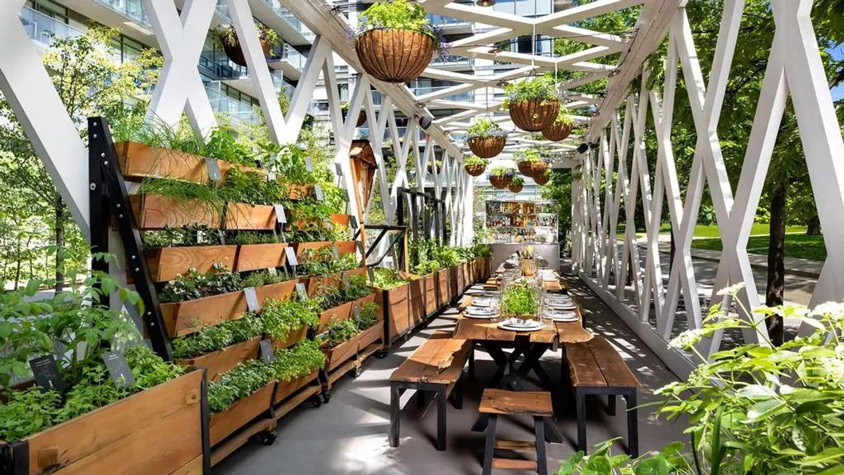 A dining room table at a 1 Hotels property is surrounded by wooden planters full of growing herbs.