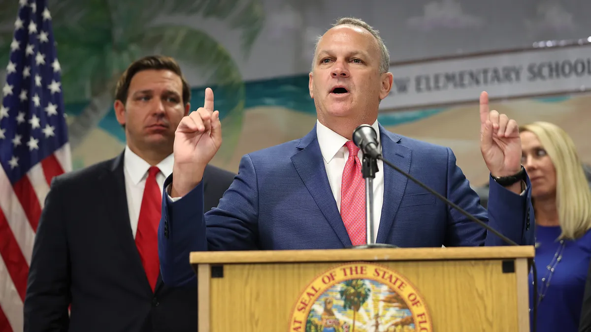 Richard Corcoran speaks at a podium with Gov. Ron DeSantis behind him.