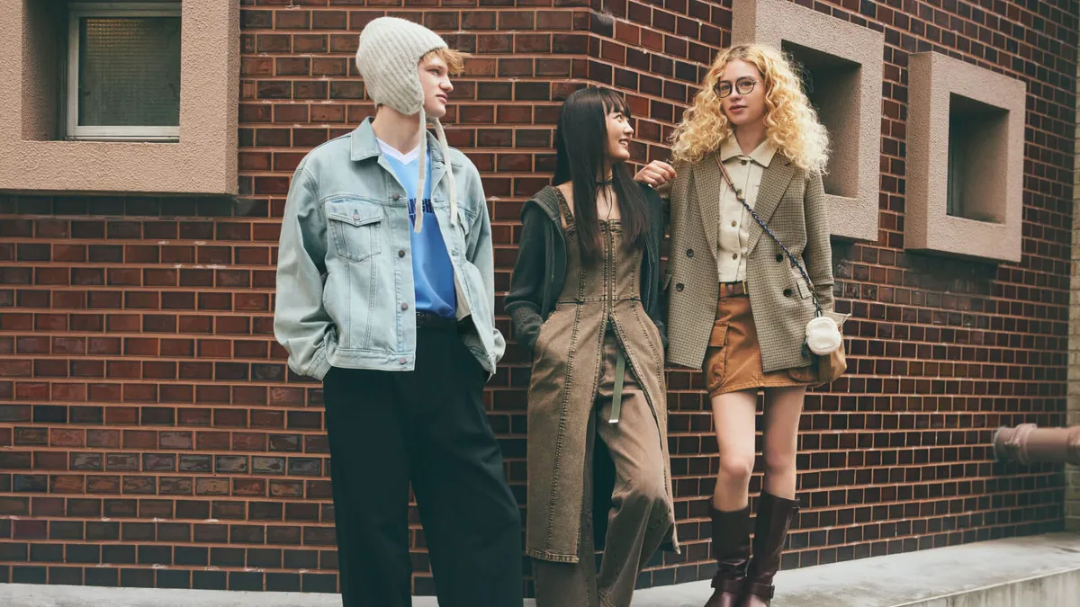 Three models stand side by side against a brick wall outdoors, wearing GU items for fall.