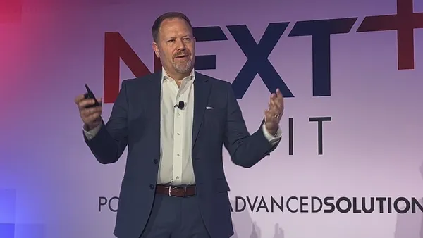 A man in a suit gives a presentation from a stage at a technology conference.