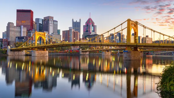 The Pittsburgh skyline is seen and buildings are reflected in the water in a river.