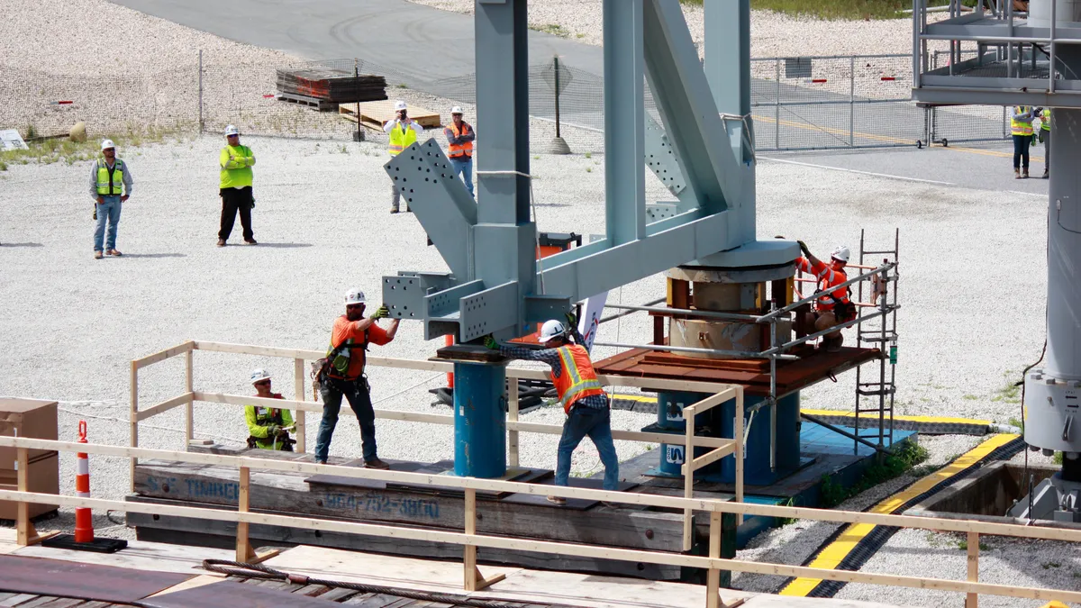 Workers in safety girl circle and perform tasks on a large iron structure.