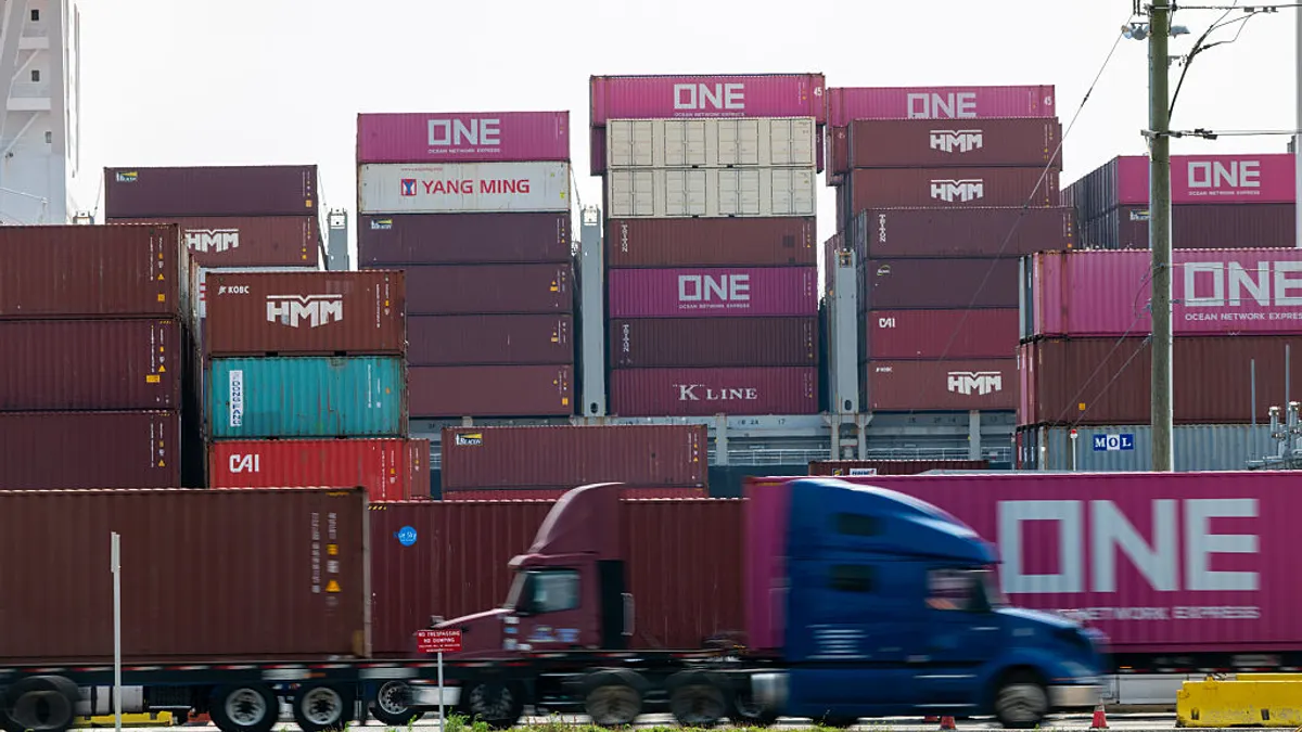 Trucks drive by cargo containers at an ocean port.