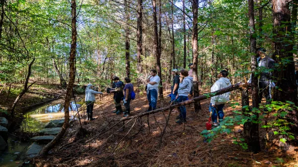Students standing in woods near a creek facing instructor.