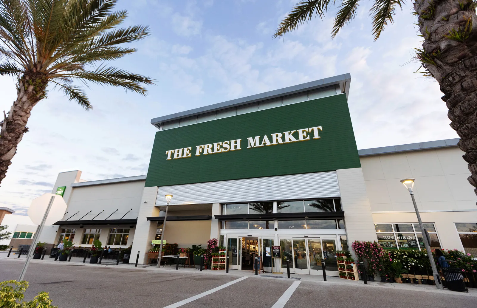 Exterior of The Fresh Market&#x27;s Lakewood Ranch store with flowers out front, palm trees and a blue sky