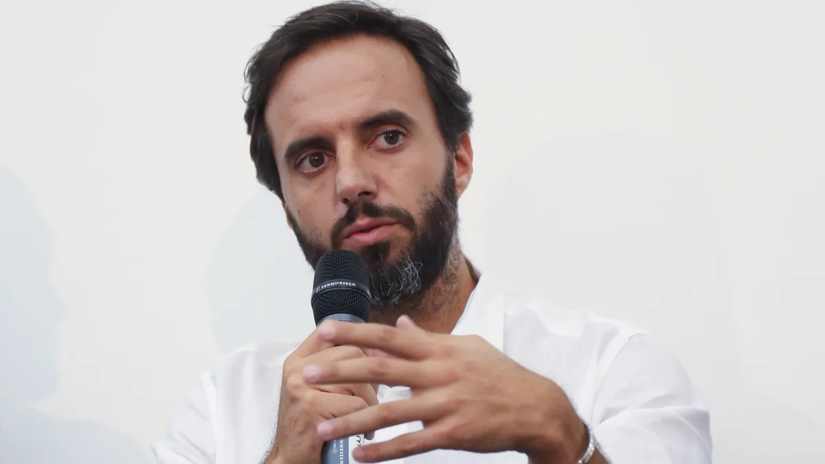 A person, Jose Neves, sits on a stage speaking into a microphone.