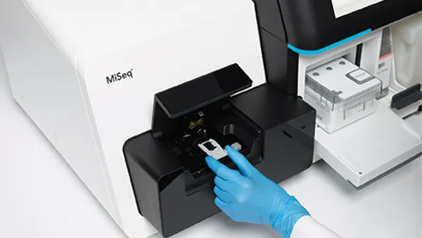 The hand of a scientist in a blue glove runs a test on an Illumina sequencing machine.